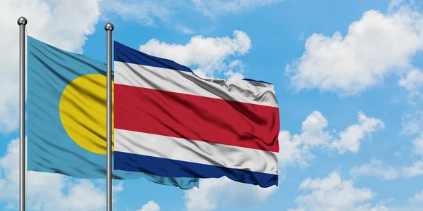 Palau e la bandiera del Costa Rica sventolano insieme nel vento contro il cielo blu nuvoloso bianco. Concetto di diplomazia, relazioni internazionali . — Foto Stock