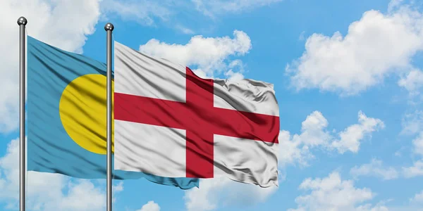 Bandera de Palaos e Inglaterra ondeando en el viento contra el cielo azul nublado blanco juntos. Concepto diplomático, relaciones internacionales . — Foto de Stock