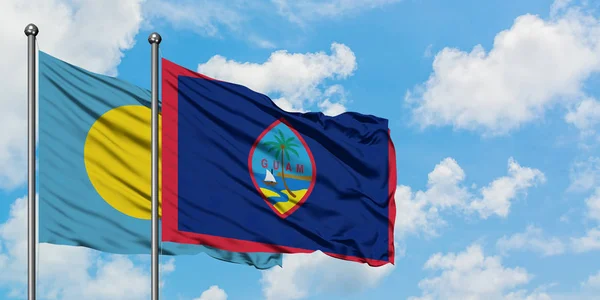 Bandera de Palau y Guam ondeando en el viento contra el cielo azul nublado blanco juntos. Concepto diplomático, relaciones internacionales . — Foto de Stock