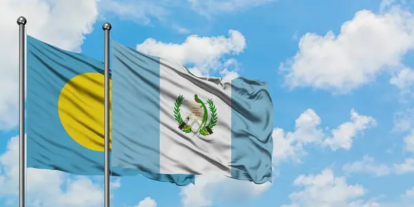 Palau e la bandiera del Guatemala sventolano nel vento contro il bianco cielo blu nuvoloso insieme. Concetto di diplomazia, relazioni internazionali . — Foto Stock