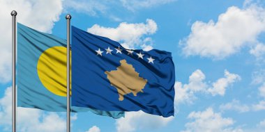 Palau ve Kosova bayrağı birlikte beyaz bulutlu mavi gökyüzüne karşı rüzgarda sallayarak. Diplomasi kavramı, uluslararası ilişkiler.