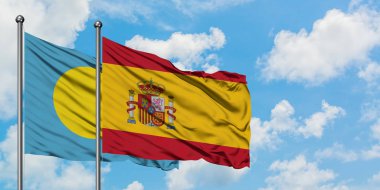 Palau ve İspanya bayrağı birlikte beyaz bulutlu mavi gökyüzüne karşı rüzgarda sallayarak. Diplomasi kavramı, uluslararası ilişkiler.