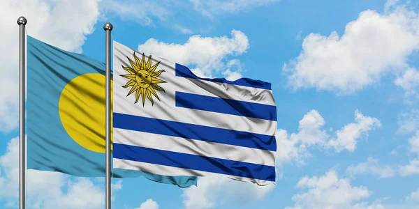 Bandera de Palaos y Uruguay ondeando en el viento contra el cielo azul nublado blanco juntos. Concepto diplomático, relaciones internacionales . — Foto de Stock