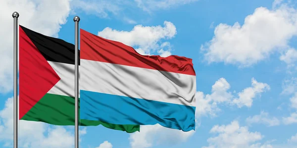 Bandera de Palestina y Luxemburgo ondeando en el viento contra el cielo azul nublado blanco juntos. Concepto diplomático, relaciones internacionales . — Foto de Stock