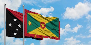 Papua Yeni Gine ve Grenada bayrağı birlikte beyaz bulutlu mavi gökyüzüne karşı rüzgarda sallayarak. Diplomasi kavramı, uluslararası ilişkiler.