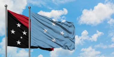 Papua Yeni Gine ve Mikronezya bayrağı birlikte beyaz bulutlu mavi gökyüzüne karşı rüzgarda sallayarak. Diplomasi kavramı, uluslararası ilişkiler.