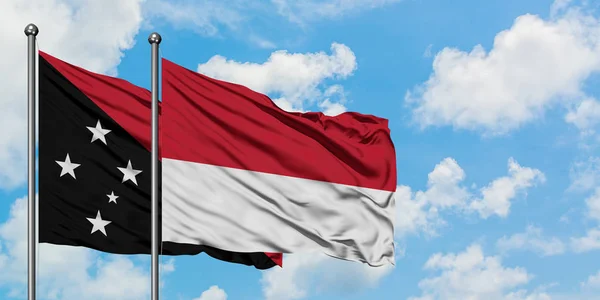 Papua Neuguinea und Monaco schwenken gemeinsam die Flagge im Wind vor dem wolkenverhangenen blauen Himmel. Diplomatie-Konzept, internationale Beziehungen. — Stockfoto