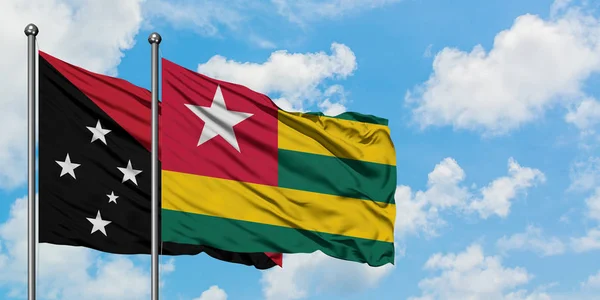 Bandera de Papúa Nueva Guinea y Togo ondeando en el viento contra el cielo azul nublado blanco juntos. Concepto diplomático, relaciones internacionales . — Foto de Stock