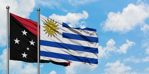 Bandera de Papúa Nueva Guinea y Uruguay ondeando en el viento contra el cielo azul nublado blanco juntos. Concepto diplomático, relaciones internacionales . —  Fotos de Stock