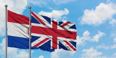 Paraguay ve Birleşik Krallık bayrağı birlikte beyaz bulutlu mavi gökyüzüne karşı rüzgarda sallayarak. Diplomasi kavramı, uluslararası ilişkiler.