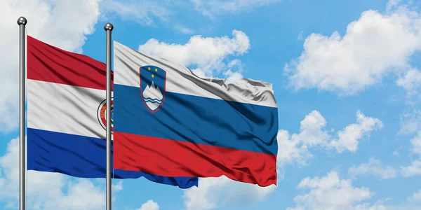 Die Flagge Paraguays und Sloweniens weht gemeinsam im Wind vor dem wolkenverhangenen blauen Himmel. Diplomatie-Konzept, internationale Beziehungen. — Stockfoto