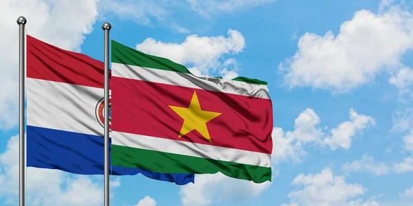 Bandera de Paraguay y Surinam ondeando en el viento contra el cielo azul nublado blanco juntos. Concepto diplomático, relaciones internacionales . — Foto de Stock