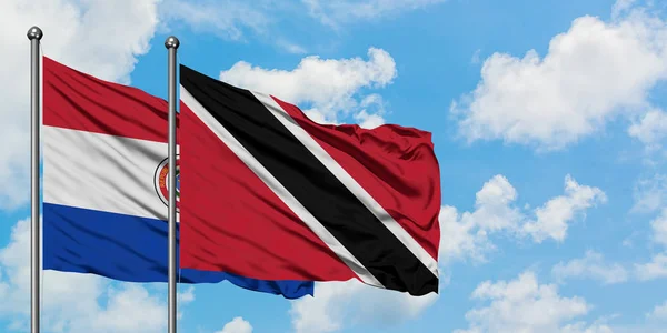 Bandera de Paraguay y Trinidad y Tobago ondeando en el viento contra el cielo azul nublado blanco juntos. Concepto diplomático, relaciones internacionales . — Foto de Stock