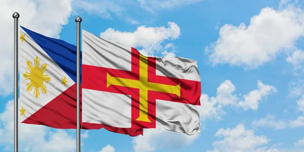 Bandera de Filipinas y Guernsey ondeando en el viento contra el cielo azul nublado blanco juntos. Concepto diplomático, relaciones internacionales . — Foto de Stock