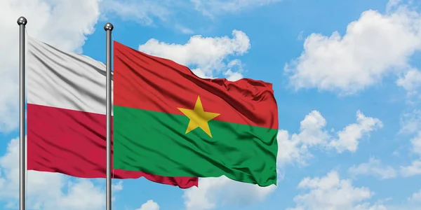 Bandera de Polonia y Burkina Faso ondeando en el viento contra el cielo azul nublado blanco juntos. Concepto diplomático, relaciones internacionales . — Foto de Stock