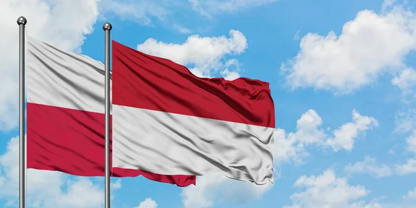 ポーランドとインドネシアの旗は、一緒に白い曇り青い空に対して風に手を振る。外交概念、国際関係. — ストック写真