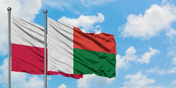 Drapeau de la Pologne et de Madagascar agitant dans le vent contre ciel bleu nuageux blanc ensemble. Concept de diplomatie, relations internationales . — Photo