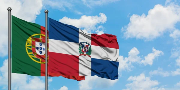 Bandera de Portugal y República Dominicana ondeando en el viento contra el cielo azul nublado blanco juntos. Concepto diplomático, relaciones internacionales . — Foto de Stock