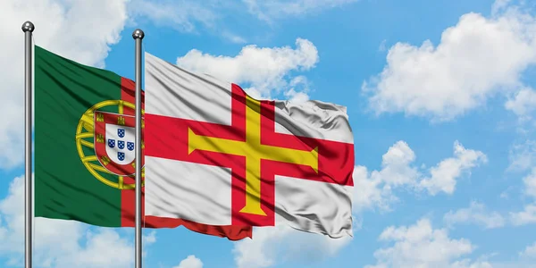 Portogallo e bandiera Guernsey sventolano insieme nel vento contro il bianco cielo blu nuvoloso. Concetto di diplomazia, relazioni internazionali . — Foto Stock