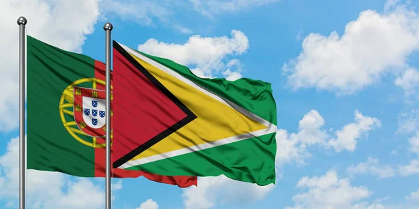 Bandera de Portugal y Guyana ondeando en el viento contra el cielo azul nublado blanco juntos. Concepto diplomático, relaciones internacionales . — Foto de Stock