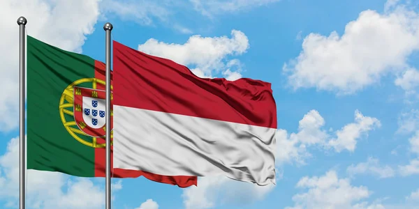 一緒に白い曇り青い空に対して風に手を振るポルトガルとインドネシアの旗。外交概念、国際関係. — ストック写真
