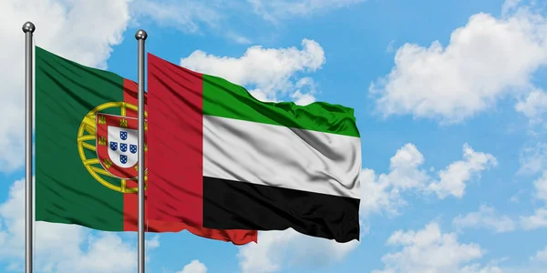 Португалия и Объединенные Арабские Эмираты вместе размахивают флагом на ветру против белого облачного голубого неба. Концепция дипломатии, международные отношения . — стоковое фото