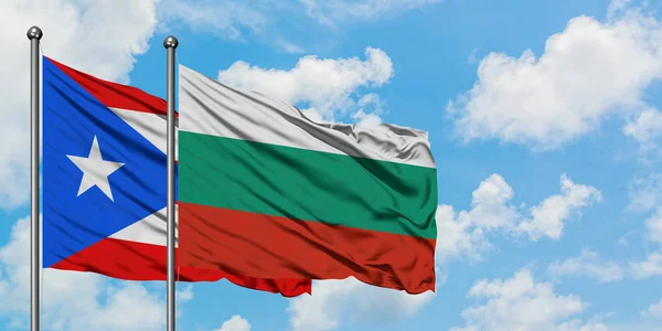 Bandera de Puerto Rico y Bulgaria ondeando en el viento contra el cielo azul nublado blanco juntos. Concepto diplomático, relaciones internacionales . — Foto de Stock
