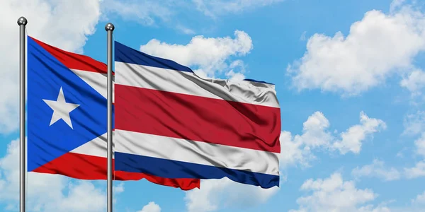 Пуерто-Ріко і Коста-Ріка прапор розмахуючи в вітру проти білого хмарного синього неба разом. Концепція дипломатії, міжнародні відносини. — стокове фото