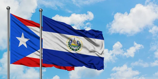 Bandera de Puerto Rico y El Salvador ondeando en el viento contra el cielo azul nublado blanco juntos. Concepto diplomático, relaciones internacionales . — Foto de Stock