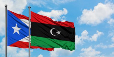 Porto Riko ve Libya bayrağı birlikte beyaz bulutlu mavi gökyüzüne karşı rüzgarda sallayarak. Diplomasi kavramı, uluslararası ilişkiler.