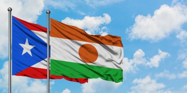 Porto Riko ve Nijer bayrağı birlikte beyaz bulutlu mavi gökyüzüne karşı rüzgarda sallayarak. Diplomasi kavramı, uluslararası ilişkiler.