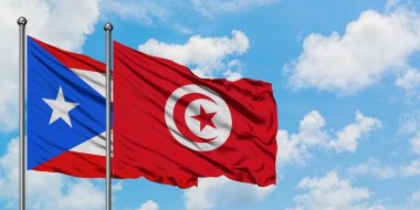 Porto Riko ve Tunus bayrağı birlikte beyaz bulutlu mavi gökyüzüne karşı rüzgarda sallayarak. Diplomasi kavramı, uluslararası ilişkiler.