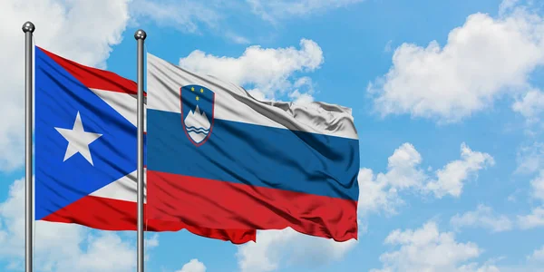 Puerto Rico and Slovenia flag waving in the wind against white cloudy blue sky together. Diplomacy concept, international relations.