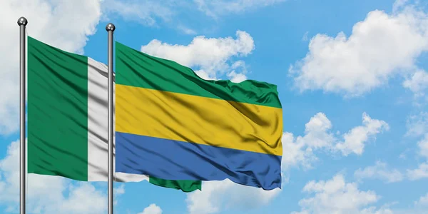 Nigeria en Gabon vlag zwaaien in de wind tegen witte bewolkte blauwe hemel samen. Diplomatie concept, internationale betrekkingen. — Stockfoto