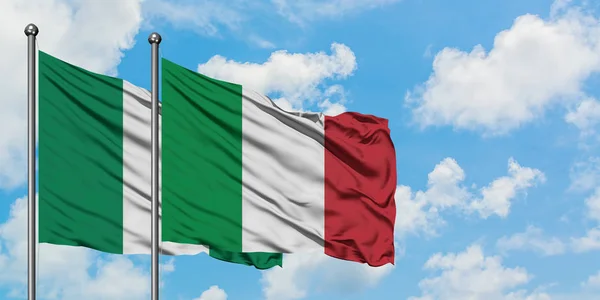 Nigeria och Italien flagga vinka i vinden mot vit grumlig blå himmel tillsammans. Diplomatisk koncept, internationella relationer. — Stockfoto