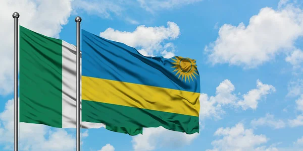 Bandera de Nigeria y Ruanda ondeando en el viento contra el cielo azul nublado blanco juntos. Concepto diplomático, relaciones internacionales . — Foto de Stock