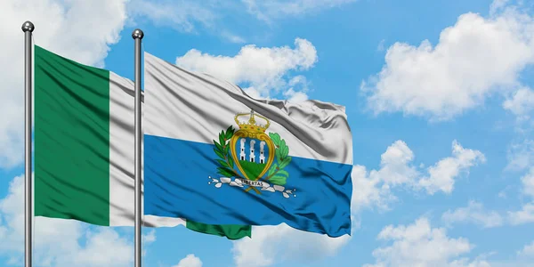 Bandera de Nigeria y San Marino ondeando en el viento contra el cielo azul nublado blanco juntos. Concepto diplomático, relaciones internacionales . — Foto de Stock