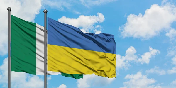 Nigerijská a ukrajinská vlajka mávali ve větru proti bíle zatažené modré obloze. Diplomacie, mezinárodní vztahy. — Stock fotografie