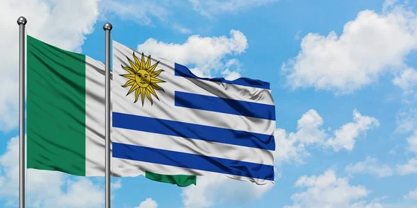 Nigeria und Uruguay schwenken gemeinsam die Flagge im Wind vor dem wolkenverhangenen blauen Himmel. Diplomatie-Konzept, internationale Beziehungen. — Stockfoto