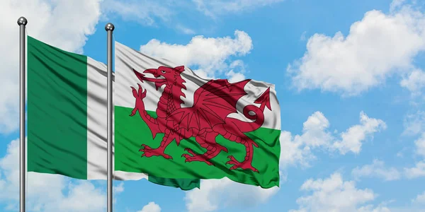 A bandeira da Nigéria e do País de Gales agitando no vento contra o céu azul nublado branco juntos. Conceito de diplomacia, relações internacionais . — Fotografia de Stock