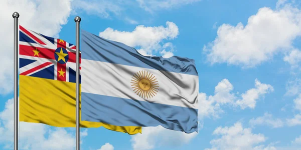 Bandera de Niue y Argentina ondeando en el viento contra el cielo azul nublado blanco juntos. Concepto diplomático, relaciones internacionales . — Foto de Stock