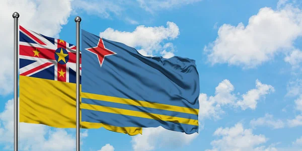 Niue és Aruba zászló integetett a szél ellen, fehér felhős kék ég együtt. Diplomáciai koncepció, nemzetközi kapcsolatok. — Stock Fotó