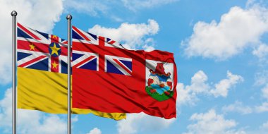 Niue ve Bermuda bayrağı birlikte beyaz bulutlu mavi gökyüzüne karşı rüzgarda sallayarak. Diplomasi kavramı, uluslararası ilişkiler.