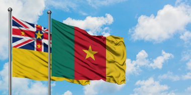 Niue ve Kamerun bayrağı birlikte beyaz bulutlu mavi gökyüzüne karşı rüzgarda sallayarak. Diplomasi kavramı, uluslararası ilişkiler.