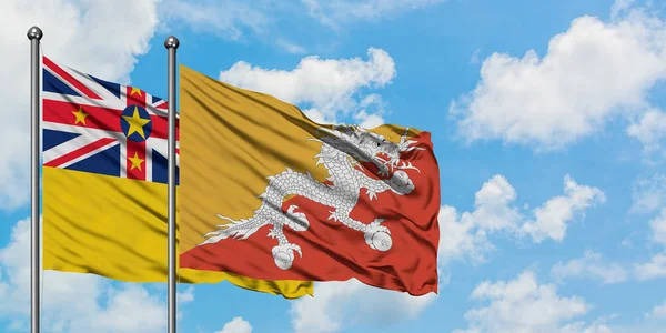 Bandera de Niue y Bután ondeando en el viento contra el cielo azul nublado blanco juntos. Concepto diplomático, relaciones internacionales . — Foto de Stock