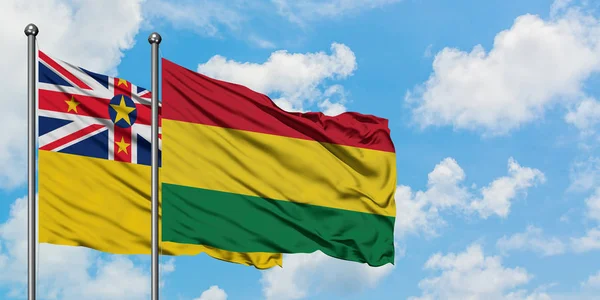 Bandera de Niue y Bolivia ondeando en el viento contra el cielo azul nublado blanco juntos. Concepto diplomático, relaciones internacionales . — Foto de Stock