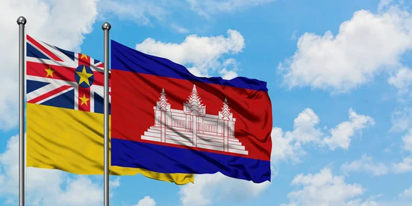 Bandera de Niue y Camboya ondeando en el viento contra el cielo azul nublado blanco juntos. Concepto diplomático, relaciones internacionales . — Foto de Stock