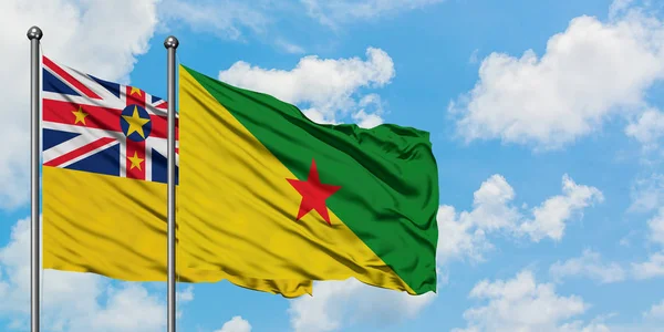 Bandera de Niue y Guayana Francesa ondeando en el viento contra el cielo azul nublado blanco juntos. Concepto diplomático, relaciones internacionales . — Foto de Stock