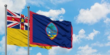 Niue ve Guam bayrağı birlikte beyaz bulutlu mavi gökyüzüne karşı rüzgarda sallayarak. Diplomasi kavramı, uluslararası ilişkiler.