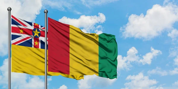 Bandera de Niue y Guinea ondeando en el viento contra el cielo azul nublado blanco juntos. Concepto diplomático, relaciones internacionales . — Foto de Stock